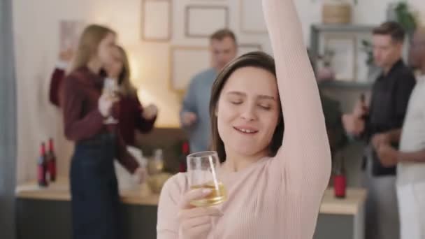 在家庭聚会的镜头前 拿着一杯白葡萄酒跳舞的快乐年轻女子的中影 背景下聚会的人群 — 图库视频影像
