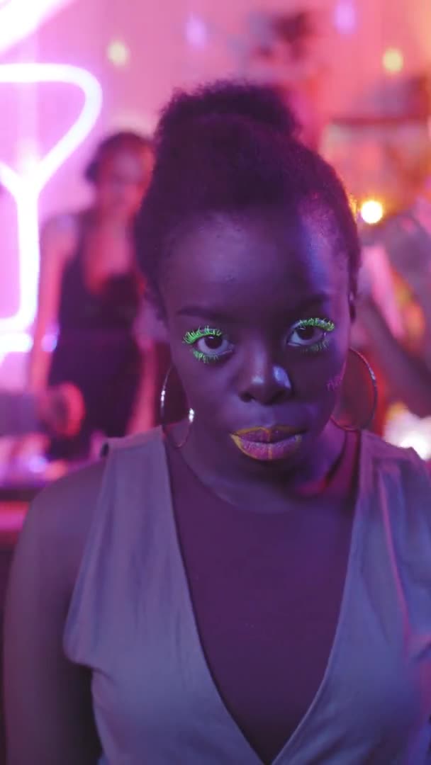 在派对上 一个年轻的黑人女人带着充满活力的妆容和耳环对着相机微笑的垂直镜头 — 图库视频影像