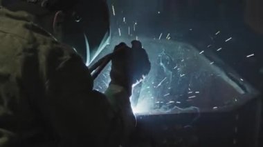 Koruyucu iş giysisi ve yüz kalkanı takmış, çelik ve diğer metalleri kaynak yaparken omzunun üstünden vurularak tanınmaz hale gelmiş.