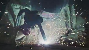 Tanımlanamayan bir adam traktör fabrikasında kaynakçı olarak çalışıyor koruyucu kostüm ve yüz kalkanı kaynaklama metali giyiyor.