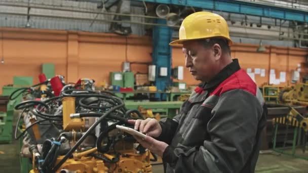 大型牵引机装配厂机械设备检测中使用数字平板技术对黄帽男厂长的中照 — 图库视频影像