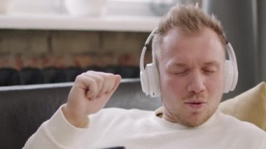 Kulaklıklı kaygısız bir gencin cep telefonu tutarken ve gözleri kapalı kanepede dinlenirken müziğin keyfini çıkartırken yakın plan çekimi.