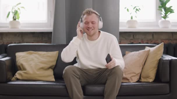 Średnie Ujęcie Młodego Mężczyzny Słuchawkach Trzymającego Telefon Komórkowy Cieszącego Się — Wideo stockowe