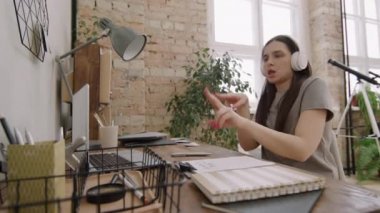 Kulaklıklı, enerjik genç bir kadının dairesindeki masasında otururken dizüstü bilgisayarında dans edip müzik videosu izlediği orta boy bir fotoğraf.