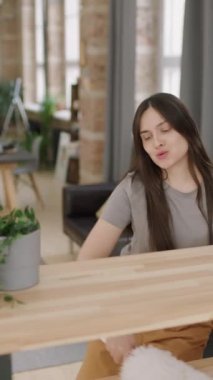 Evini temizlerken rafların tozunu alan, dans eden ve şarkı söyleyen mutlu genç bir kadının dikey portresi.