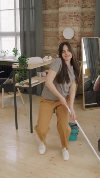 一个精力充沛的年轻女子在公寓里扫地 在镜头前跳舞的垂直镜头 — 图库视频影像