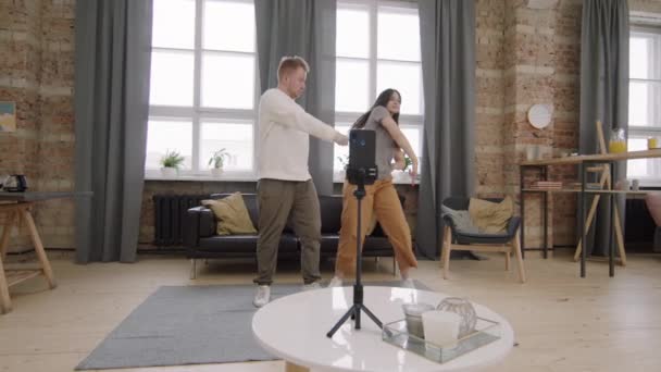 若い男性と女性が一緒に踊り 三脚の上で携帯電話で自分自身を撮影のスローモーション追跡ショット — ストック動画