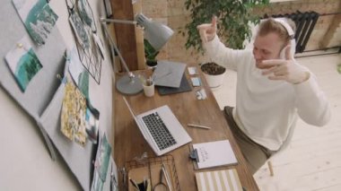 Kulaklıklı mutlu bir gencin dairede oturmuş dizüstü bilgisayarında müzik videosu izlediği en iyi görüntü. Müziğe yöneliyor ve gülümsüyor.