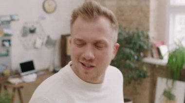 Kameraya poz veren ve dairesinde dans eden mutlu genç adamın portresi.