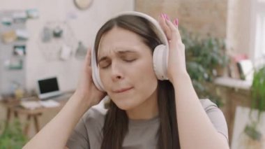 Kulaklıklı genç bir kadının kameradan önce şarkı söyleyip müzik dinlediği yakın çekim.