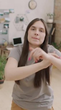 Müzik eşliğinde dans ederken gülümseyen ve kameraya bakan güzel bir genç kadının dikey portresi.