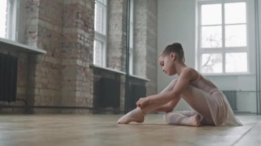 9 yaşındaki güzel balerin boş bir bale stüdyosunun zemininde otururken ayak parmağı ayakkabısı giyerken sonra ayağa kalkıp zarif bir şekilde bale yapmaya başlarken.