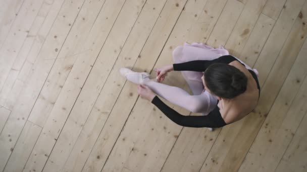 芭蕾训练前 身着黑色紧身衣 开著背坐在木制地板上的年轻而优雅的芭蕾舞演员的头像镜头 — 图库视频影像