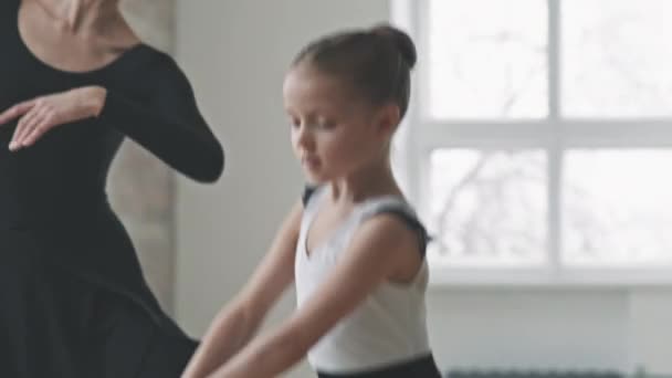 跟踪身穿黑色芭蕾舞裙的年轻专业芭蕾舞演员与漂亮小女孩合唱的腰部合影 在舞蹈课上步调一致 — 图库视频影像