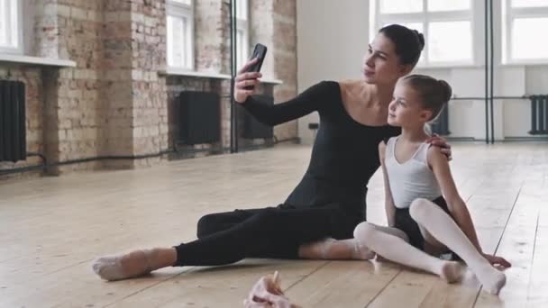 芭蕾舞课后 两名漂亮的高加索成年人和年轻的芭蕾舞演员坐在舞蹈学校的木制地板上 用智能手机自拍 — 图库视频影像