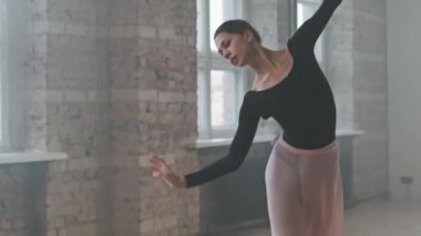 Boş bale sınıfında dans eden siyah elbiseli, orta boy, genç balerin koreografisini prova ediyor.