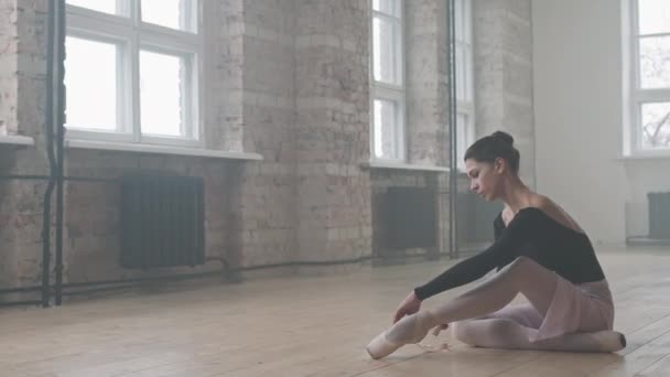 在跳芭蕾舞之前 身穿黑色紧身衣的年轻优雅芭蕾舞演员坐在木制地板上 手握编舞鞋的Pan镜头 — 图库视频影像