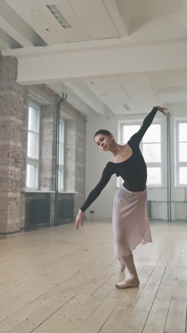 身着黑色紧身衣独自在芭蕾舞演播室里跳舞的年轻而纤细的芭蕾舞演员的垂直全景 — 图库视频影像