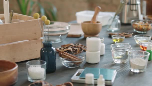 天然の手作り石鹸を作るために使用されるテーブルの上に置く油 スパイス ドライフルーツや花と様々なガラスボウルのPanショット — ストック動画