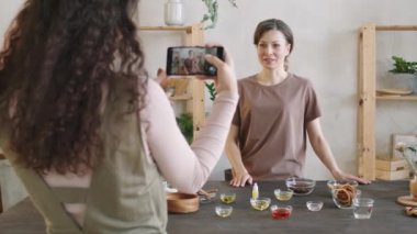 Omzunun üstünden, uzun kıvırcık saçlı, akıllı telefonlu bir kadının doğal organik sabun yapmasını anlatan videosunu çekerken.