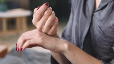 Tanımlanamayan bir kadının evde yatağında otururken ellerine krem sürmesi.