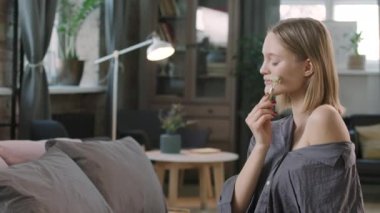 PAN belden yukarısında, kusursuz ciltli güzel bir kadının doğal kuvars pateniyle yüz masajı yaparken gülümsemesi evde rahat bir yatakta oturuyor.