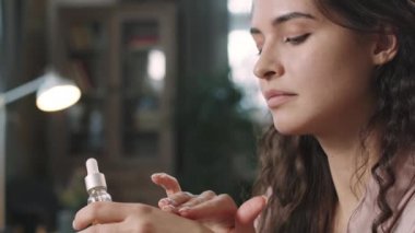 Bezelye büyüklüğünde nemlendirici doğal serumu, berrak yüzünde hyaluronik asitle uygulayan çekici genç kadının yavaş çekimleri.