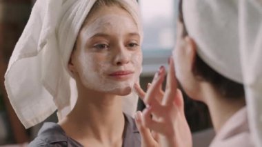 Kafkasyalı genç bir kadın ve en yakın arkadaşının birlikte güzellik prosedürü uygulayarak yüzlerine kilden maske takmalarına yakından bakın.