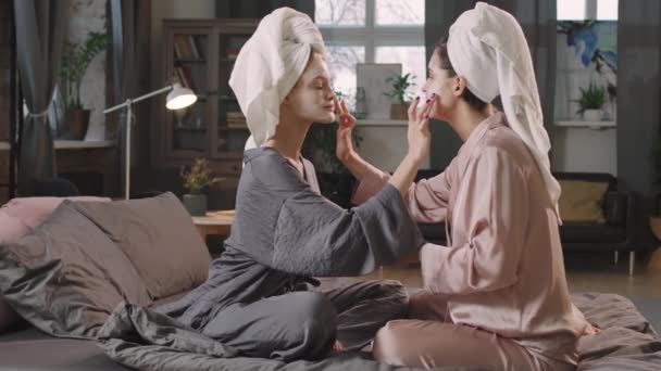 中Pan镜头 年轻的女性朋友穿着丝质睡衣 头戴白色毛巾 缓缓地坐在床上 面面相觑 一起做美容手术 — 图库视频影像