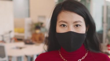 İş yerinde kameraya poz veren yüzü maskeli güzel Asyalı bir kadının portre çekimi.