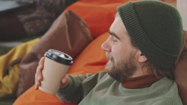 Bereli neşeli sakallı adamı yakın plan çek. Fasulye sırtına yaslan ve kahve iç.