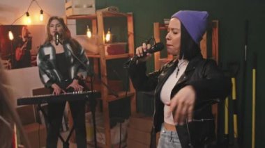 Müzik çalan, dans eden, deri ceketli, mor şapkalı çekici vokalist ve mikrofonla mikrofon çalan genç bayan rock müzik grubunun el kamerasındaki yavaşlığı.