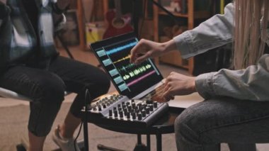 Tanımlanamayan iki kızın orta bölüm yavaşlaması rahat bir retro-stil müzik stüdyosunda oturup yeni şarkılar kaydetmeleri dizüstü bilgisayardaki ses dalgalarını ve müzik kontrol panelini gösteriyor.