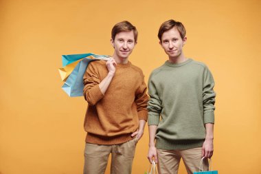 Portakal rengi arka planda alışveriş torbalarıyla duran gülümseyen genç kızların portresi.