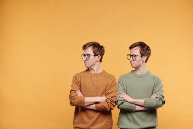 Gözlüklü, parlak kazaklı, çapraz kollu ve turuncu arka planda duran genç kızlar.