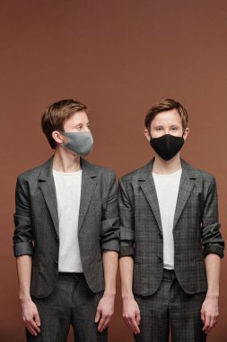 Zeki, sıradan takım elbiseli genç adam kahverengi arka planda duruyor ve siyah maskeli ergen kardeşe bakıyor.