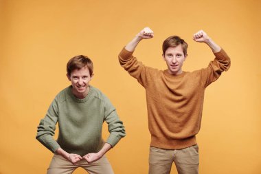 Normal süveter giyen, turuncu arka planda kaslarını esneten pozitif anlamlı güçlü gençlerin portresi.