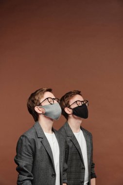 Bez maskeli ve gözlüklü iki ergen kardeş Coronavirus kısıtlamaları sırasında gözlerini kapalı ve kahverengi arka planda duruyorlar.
