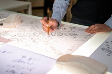 Masada duran ve araba parçası çizen tanınmayan kadın araç tasarımcısının yakın çekimi.