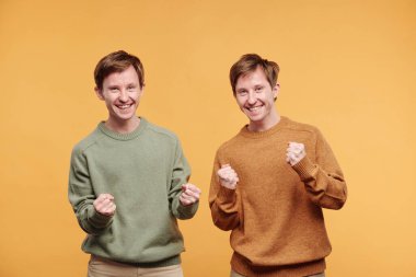 Portakal rengi arka planda hareketler yapan, sıradan süveter giyen, duygusal heyecanlı ergen kardeşler portresi.