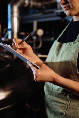 Üretim fabrikasındaki bira hazırlama aşamalarının listesini öğrenirken, önlüklü genç bir kadın panodaki belgeye işaret ediyor.