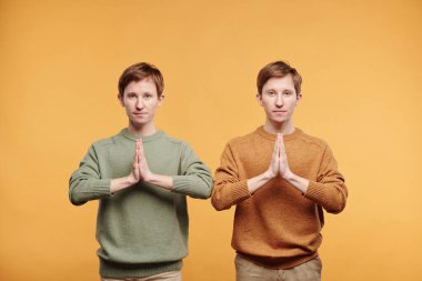 Portakal rengi arka planda duran ve Namaste 'da meditasyon yaparken el ele tutuşan, süveter giyen genç ve mutlu gençlerin portresi.