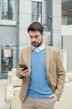 Ceketli genç hukukçu koridorda yürüyor ve telefondaki mesajları okuyor.