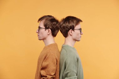 Hardallı ve zeytinli ciddi gençlerin arka planda parlak arka planda sırt sırta duran ciddi bakışları.