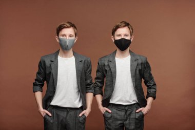 Gri takım elbiseli genç kardeşlerin portresi ve kahverengi arka planda el ele tutuşan kumaş maske.