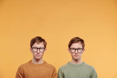 Portakal rengi arka planda duran gözlüklü ve kazaklı genç kızların portresi.