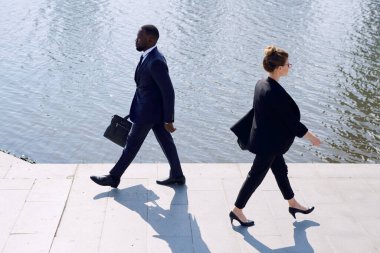 Zarif takım elbiseli genç çağdaş iş adamları işten dönerken nehir kenarında yürüyorlar.