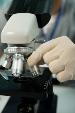 Laboratuvarda mikroskop araştırmasından önce objektif lensleri ayarlayan eldivenli tanınamayan bilim adamının yakın çekimi