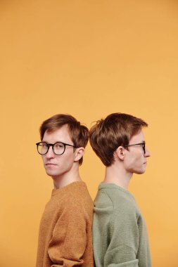 Gözlüklü, genç ve yakışıklı bir adamın portresi. Genç kardeşiyle sırt sırta, parlak arka planda.