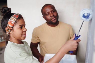Oturma odasının tuğla duvarının önünde boyayıp babasına karşı beyaz renge boyayan Afrikalı tatlı bir kız.